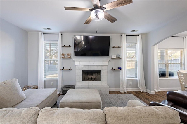 living room with ceiling fan, a fireplace, and dark wood-type flooring