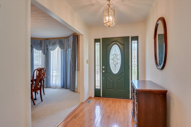 entrance foyer featuring visible vents, baseboards, light wood-style flooring, an inviting chandelier, and crown molding