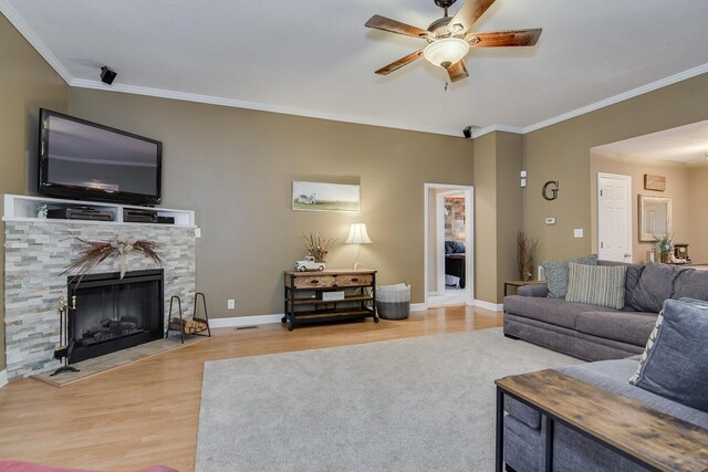 living room featuring hardwood / wood-style flooring, ceiling fan, a stone fireplace, and crown molding