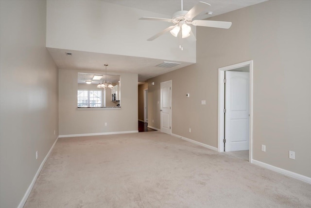 carpeted spare room featuring a towering ceiling and ceiling fan with notable chandelier