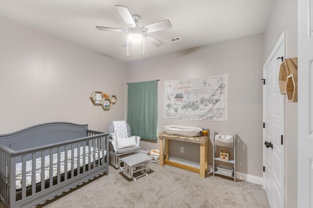 bedroom with ceiling fan, a nursery area, and light carpet