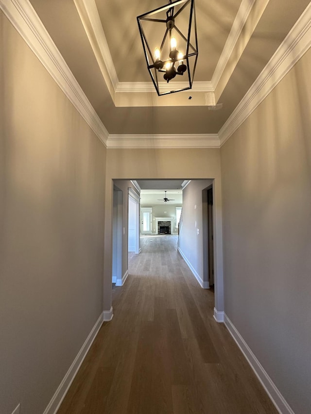 hallway featuring dark hardwood / wood-style flooring, a notable chandelier, ornamental molding, and a raised ceiling