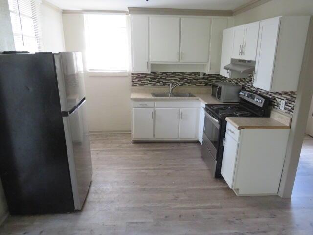 kitchen with appliances with stainless steel finishes, light wood-type flooring, white cabinetry, and sink