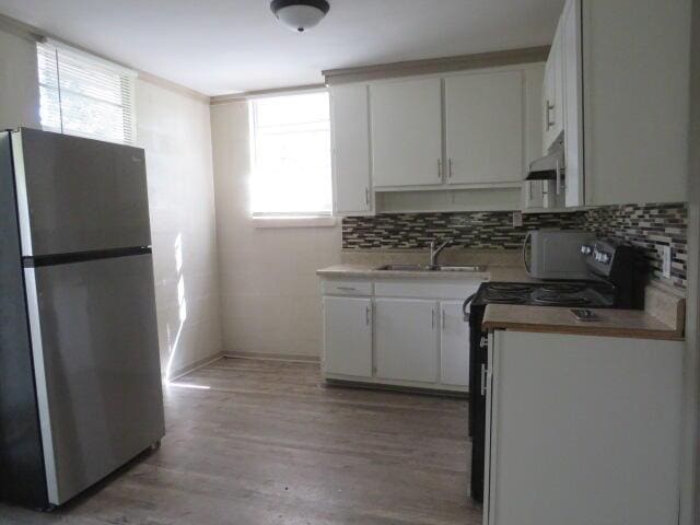 kitchen featuring black electric range, sink, white cabinets, stainless steel refrigerator, and plenty of natural light