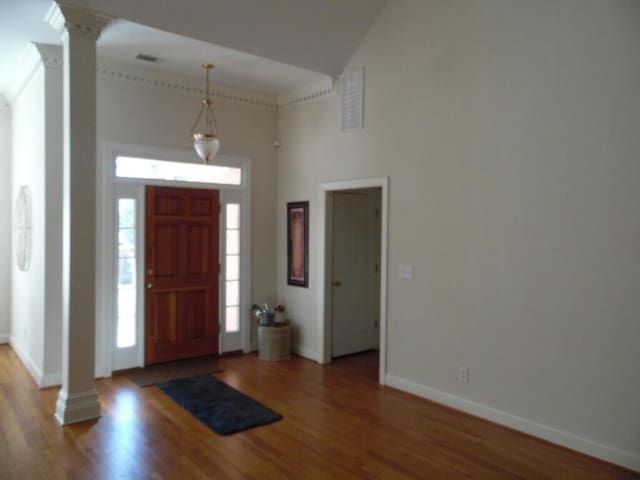 entryway with hardwood / wood-style flooring, a towering ceiling, and ornate columns