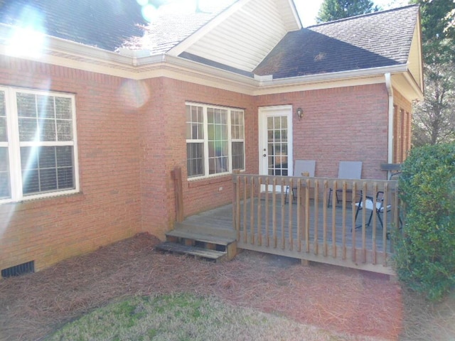 view of property exterior featuring brick siding, a shingled roof, and a deck