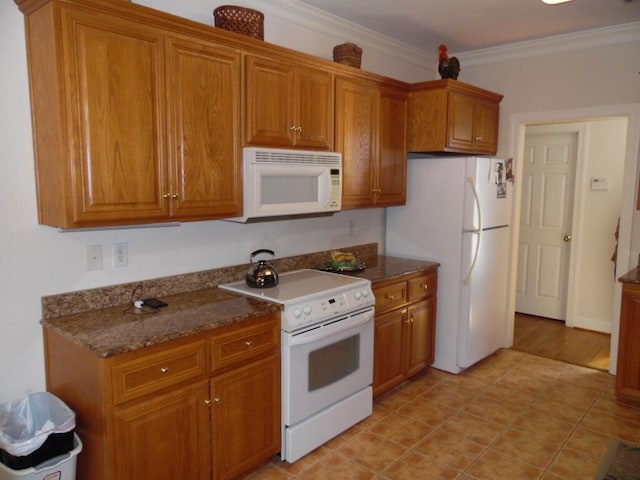 kitchen featuring ornamental molding, light tile patterned flooring, white appliances, and dark stone counters