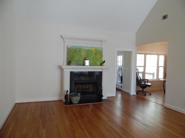 unfurnished living room featuring a tile fireplace, wood-type flooring, and high vaulted ceiling