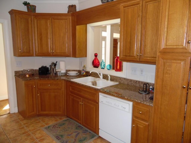 kitchen with dishwasher, a sink, brown cabinets, light tile patterned flooring, and dark stone counters