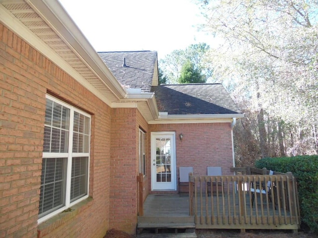 view of side of home with brick siding, a deck, and a shingled roof