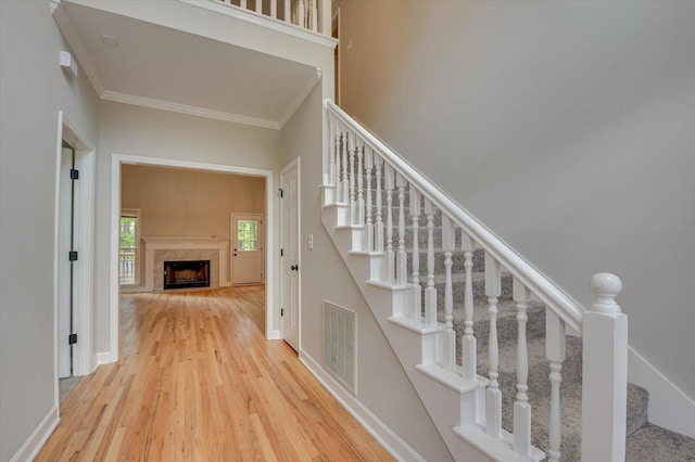 staircase featuring hardwood / wood-style floors, crown molding, and a fireplace