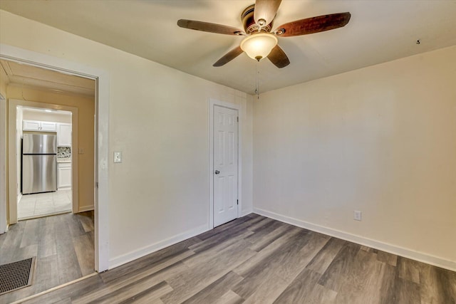 unfurnished room featuring attic access, baseboards, visible vents, wood finished floors, and ceiling fan
