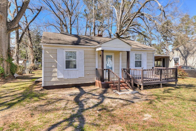 bungalow-style house featuring a wooden deck, roof with shingles, and a front lawn