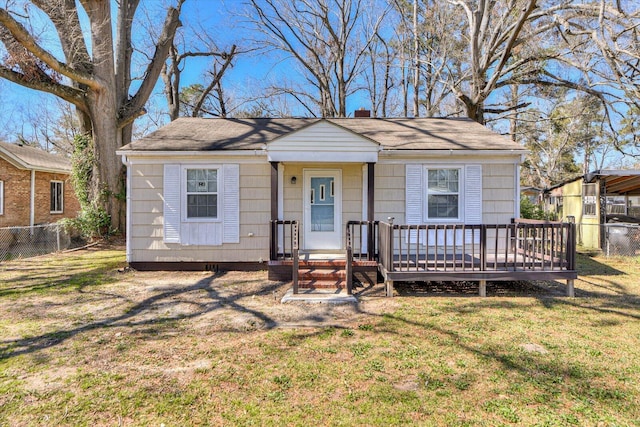 bungalow-style home with a chimney, a front lawn, fence, a wooden deck, and roof with shingles