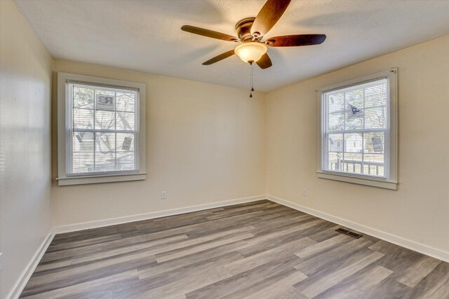 empty room with baseboards, wood finished floors, visible vents, and ceiling fan