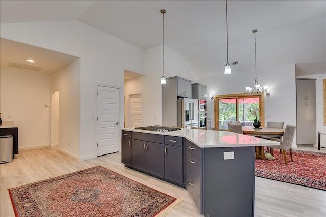 kitchen with stainless steel appliances, light countertops, a chandelier, light wood-style flooring, and high vaulted ceiling