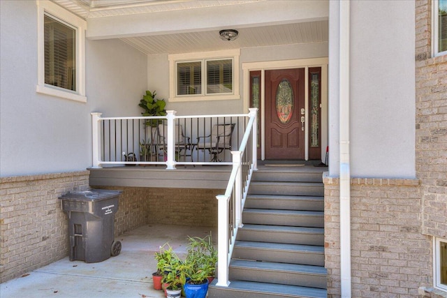 view of exterior entry featuring covered porch, brick siding, and stucco siding