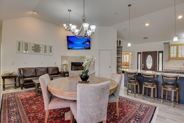 dining area with light wood-style flooring, a chandelier, a fireplace, high vaulted ceiling, and recessed lighting