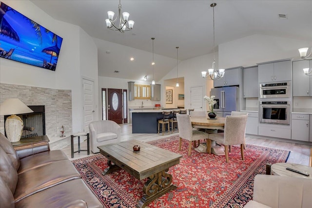 living area featuring a chandelier, light wood-type flooring, high vaulted ceiling, and a fireplace