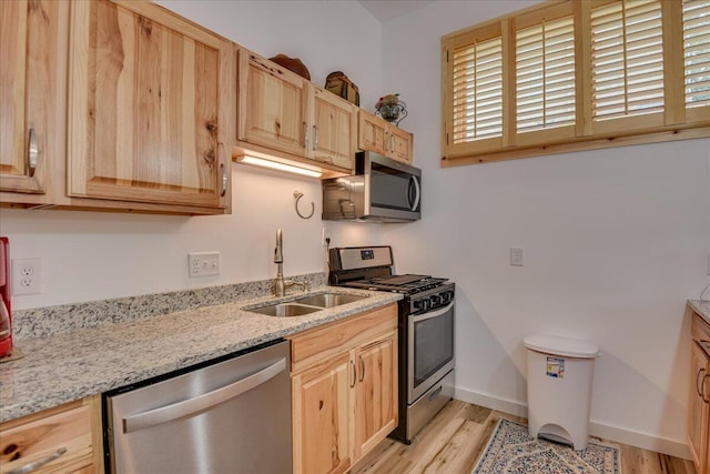 kitchen featuring stainless steel appliances, light brown cabinets, a sink, and light wood finished floors