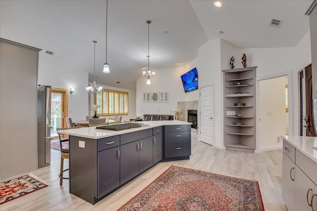 kitchen featuring a chandelier, stainless steel appliances, a kitchen island, light wood finished floors, and vaulted ceiling