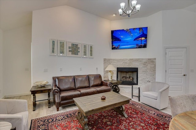 living room featuring wood finished floors, a chandelier, a stone fireplace, lofted ceiling, and baseboards