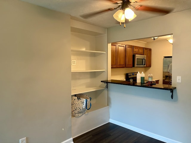 kitchen featuring appliances with stainless steel finishes, brown cabinets, dark wood-style flooring, baseboards, and a ceiling fan