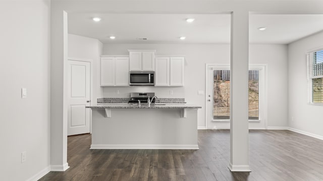 kitchen featuring appliances with stainless steel finishes, a kitchen island with sink, a kitchen breakfast bar, light stone counters, and white cabinets