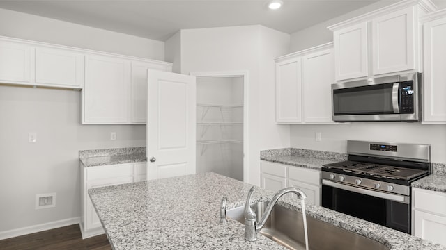 kitchen with stainless steel appliances, white cabinetry, sink, and light stone counters