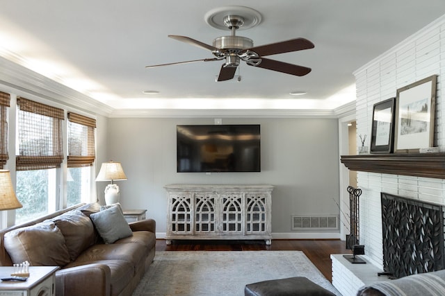 living room featuring ornamental molding, dark wood-type flooring, ceiling fan, and a fireplace