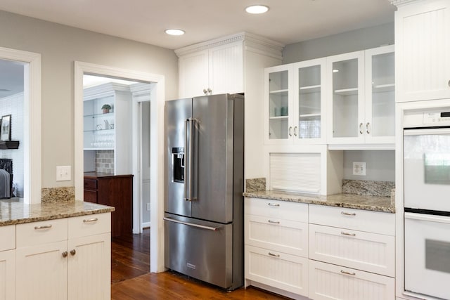 kitchen featuring high quality fridge, double oven, white cabinetry, dark hardwood / wood-style flooring, and light stone countertops