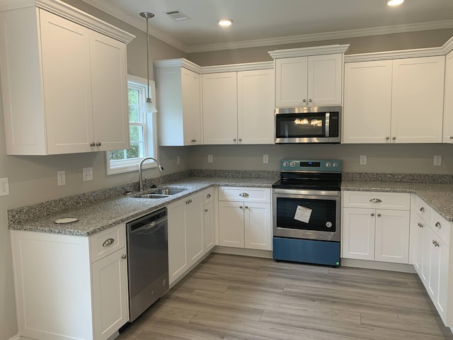 kitchen featuring light wood-style flooring, stainless steel appliances, a sink, white cabinets, and ornamental molding