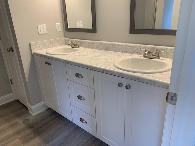 bathroom with double vanity, baseboards, a sink, and wood finished floors