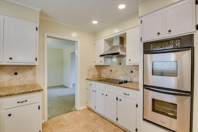 kitchen featuring wall chimney range hood, white cabinetry, double oven, light stone counters, and black electric stovetop