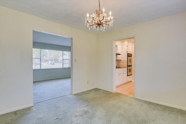 spare room featuring light colored carpet, a notable chandelier, and a textured ceiling