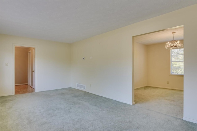 empty room with light colored carpet and a chandelier