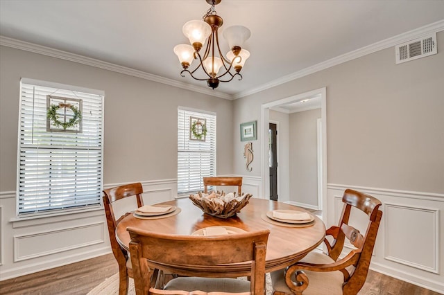 dining space with wood finished floors, a wainscoted wall, visible vents, crown molding, and a notable chandelier