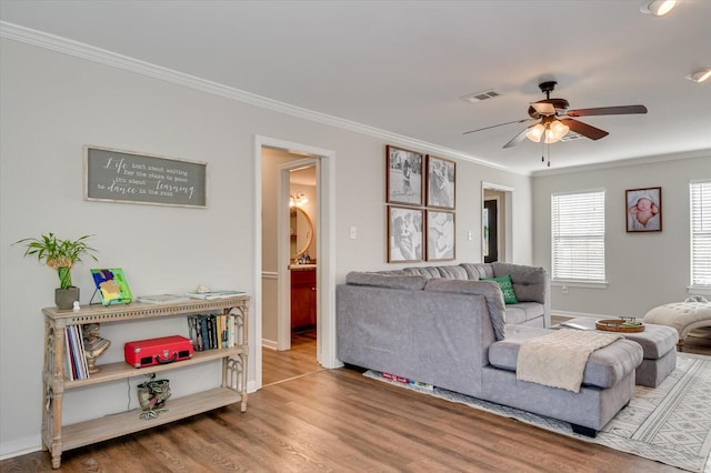 living room featuring a ceiling fan, wood finished floors, visible vents, baseboards, and crown molding