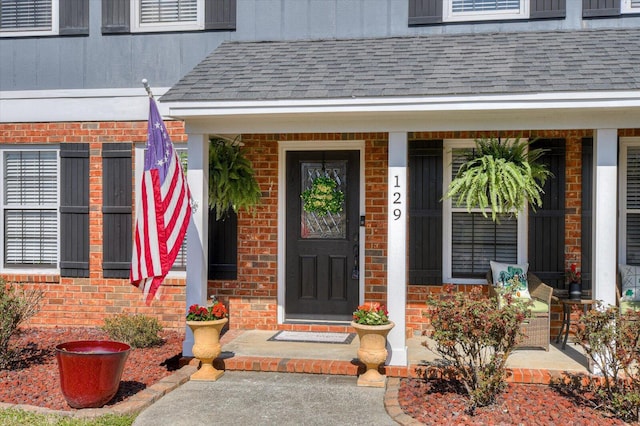 entrance to property featuring brick siding, a porch, roof with shingles, and board and batten siding