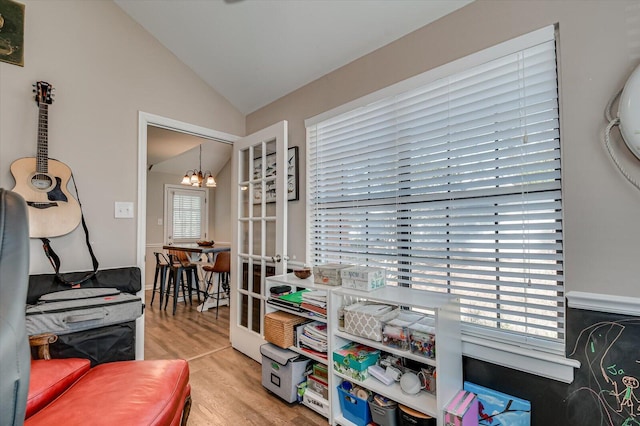 office space with a healthy amount of sunlight, wood finished floors, an inviting chandelier, and vaulted ceiling