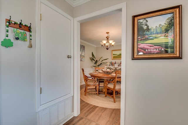 hall featuring visible vents, light wood-type flooring, an inviting chandelier, and ornamental molding