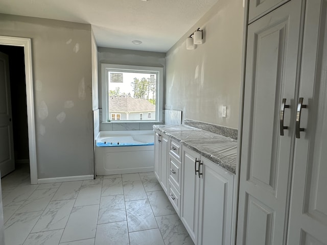 bathroom featuring vanity, baseboards, marble finish floor, and a garden tub