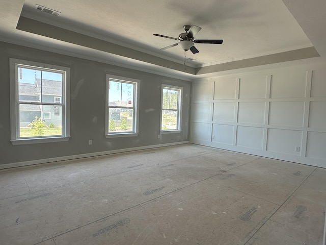 empty room with ceiling fan, a decorative wall, a tray ceiling, visible vents, and ornamental molding