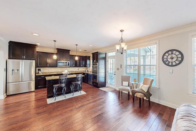 kitchen featuring decorative light fixtures, a center island, a breakfast bar, crown molding, and appliances with stainless steel finishes