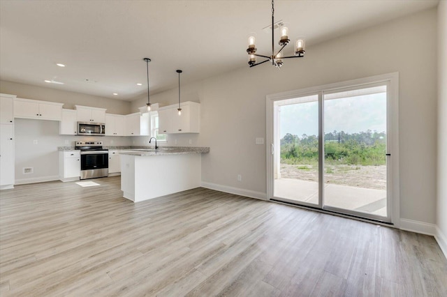 kitchen featuring kitchen peninsula, light stone counters, stainless steel appliances, pendant lighting, and white cabinetry