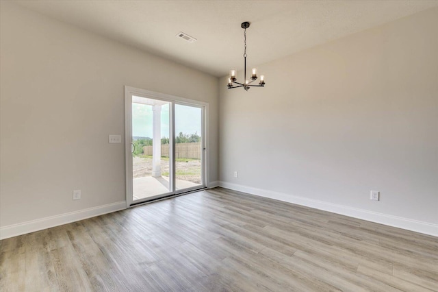 empty room with light hardwood / wood-style floors and an inviting chandelier