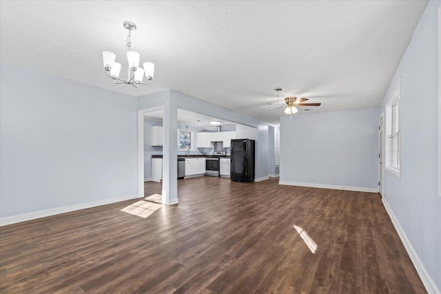 unfurnished living room featuring ceiling fan with notable chandelier, a textured ceiling, a wealth of natural light, and dark wood-type flooring