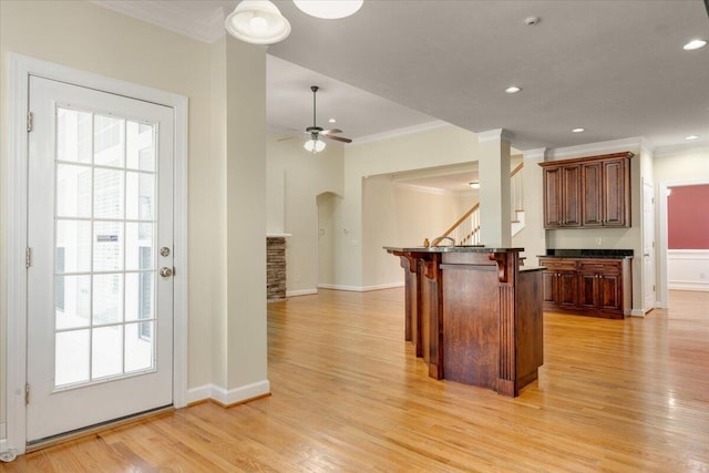 kitchen featuring a breakfast bar area, crown molding, a center island, ceiling fan, and light hardwood / wood-style floors