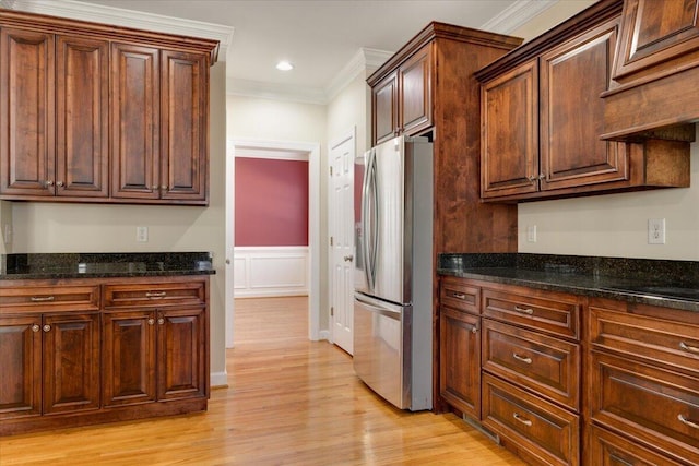 kitchen featuring stainless steel refrigerator with ice dispenser, ornamental molding, light wood-type flooring, and dark stone counters