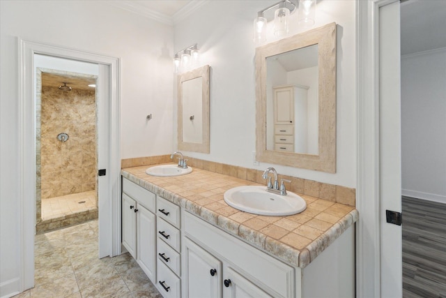 bathroom featuring double vanity, crown molding, tiled shower, and a sink